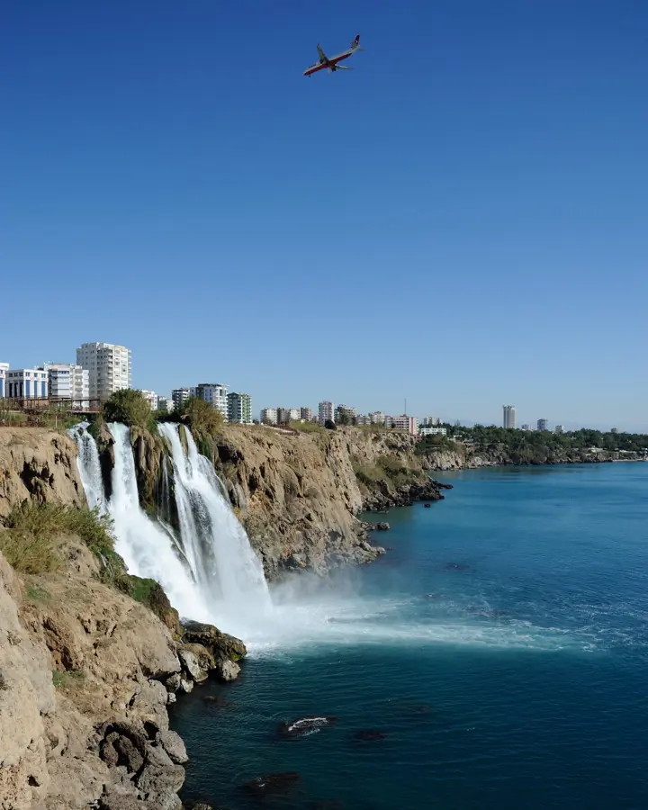 Aşağı Düden Şelalesi'nin falezlerden denize dökülüşü, arkada Antalya şehir silüeti