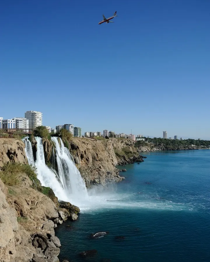 Aşağı Düden Şelalesi'nin falezlerden denize dökülüşü, arkada Antalya şehir silüeti